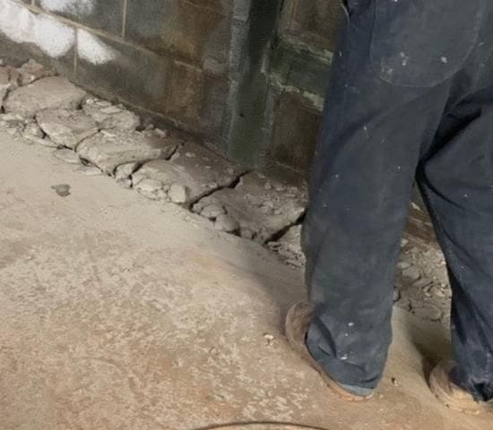 man breaking up concrete to install permanent basement waterproofing drain