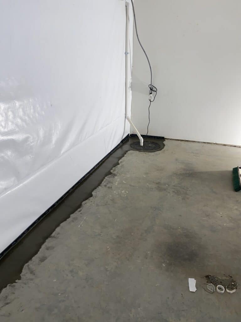 a basement after professional waterproofing, white plastic on wall, drain with fresh concrete, sump pump 