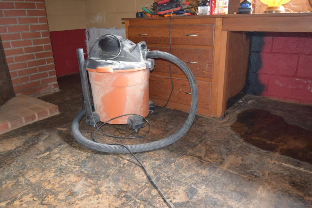 wet/dry shop vac in a basement with proof that the black tar waterproofing paint on the basement wall doesn't work, there is a puddle of water in the floor