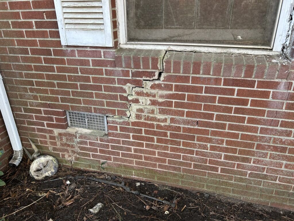 2 Pictures- First Picture is a brick house with multiple cracks leading from the window to vents and the floor. Second Image is cracks inside coming from a door heading and reaching the ceiling.